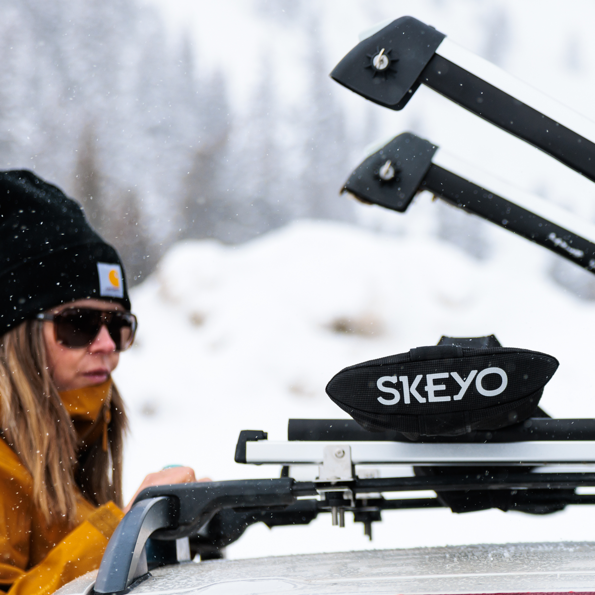 Person adjusting a SKEYO roof rack on a vehicle with a snowy background